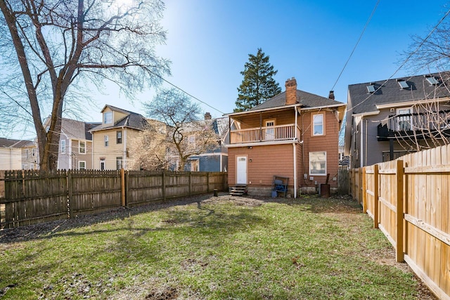 rear view of house with a balcony, a chimney, a fenced backyard, and a lawn