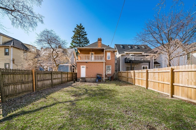 back of property featuring a lawn, entry steps, a fenced backyard, a balcony, and a chimney