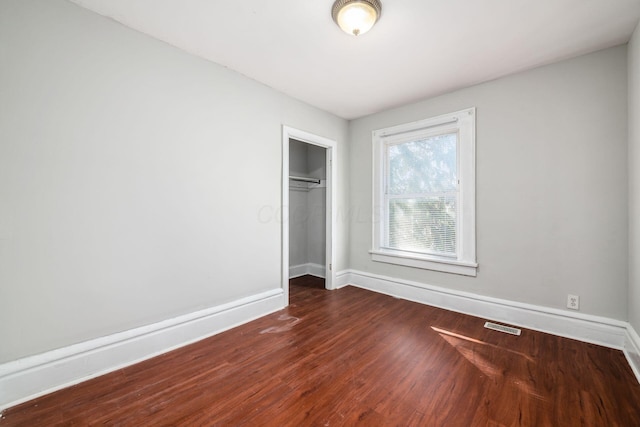 unfurnished bedroom featuring dark wood finished floors, visible vents, baseboards, and a closet