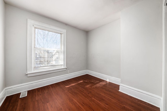 empty room with dark wood finished floors, baseboards, and visible vents