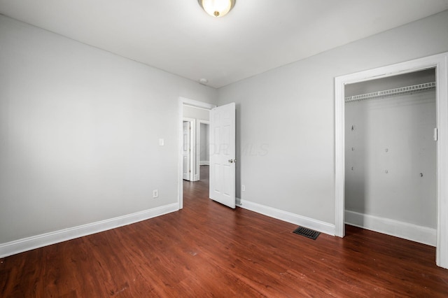 unfurnished bedroom with a closet, visible vents, baseboards, and wood finished floors