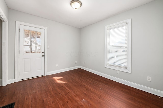 spare room with dark wood finished floors, visible vents, and baseboards