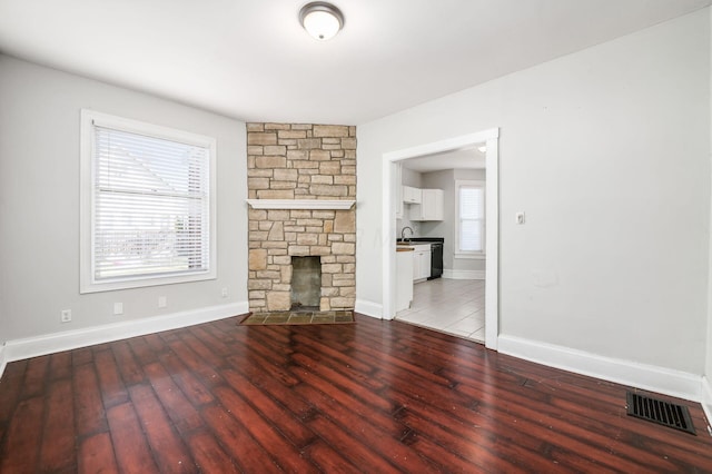 unfurnished living room with wood finished floors, visible vents, baseboards, a fireplace, and a sink