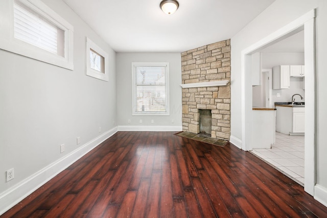 unfurnished living room with a stone fireplace, hardwood / wood-style flooring, baseboards, and a sink