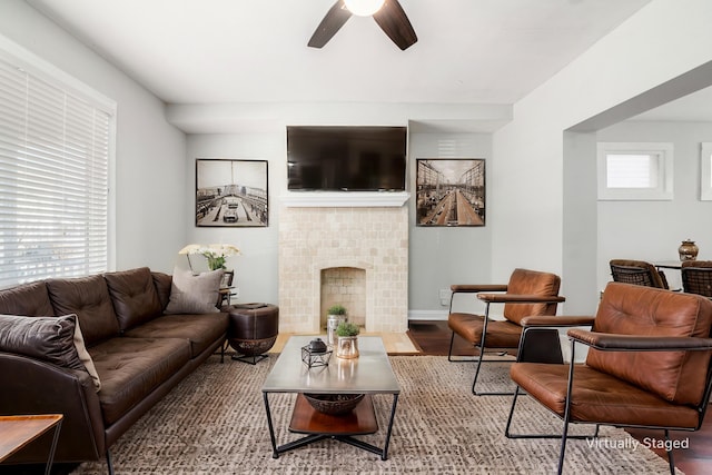 living room with baseboards, wood finished floors, a ceiling fan, and a tile fireplace