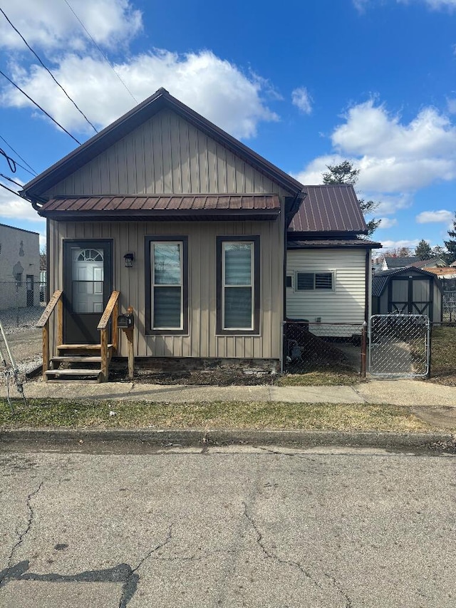 view of front of property with board and batten siding, fence, entry steps, metal roof, and a gate