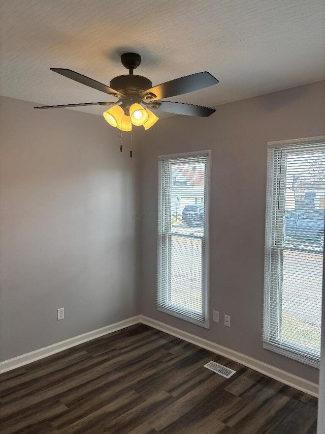 spare room with ceiling fan, visible vents, baseboards, and dark wood finished floors