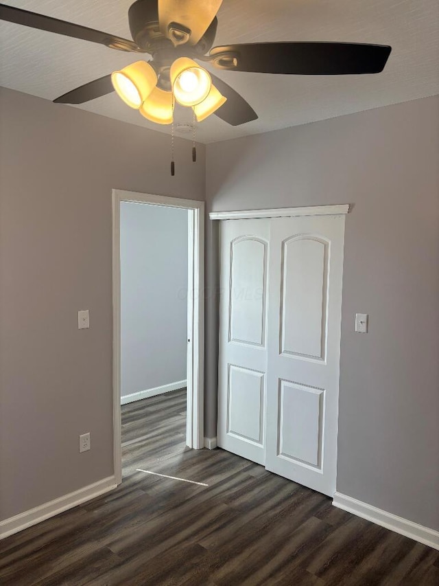 unfurnished bedroom featuring dark wood-style floors, a closet, baseboards, and a ceiling fan