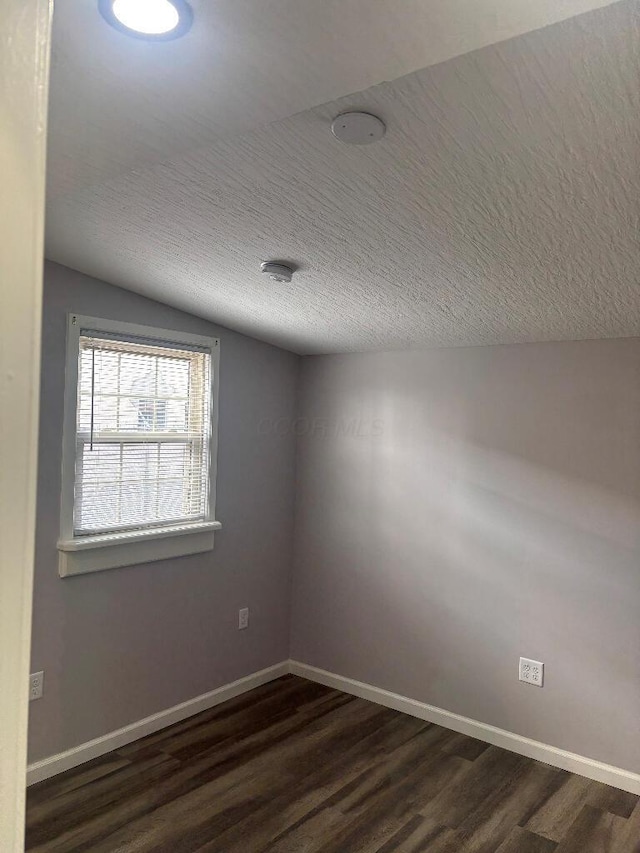 spare room with a textured ceiling, lofted ceiling, baseboards, and dark wood-style flooring