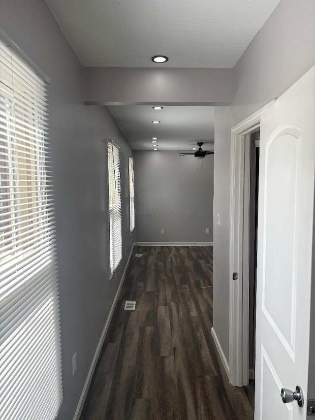 hallway featuring visible vents, dark wood-style floors, baseboards, and a wealth of natural light