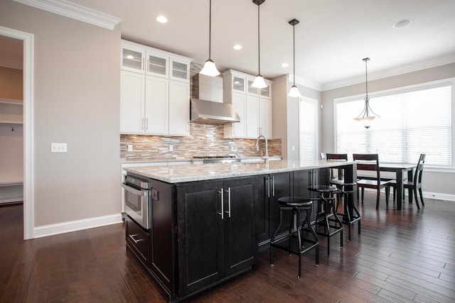 kitchen featuring an island with sink, backsplash, oven, and ornamental molding