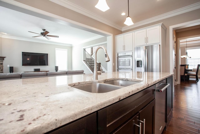 kitchen featuring dark wood-type flooring, a sink, light stone counters, appliances with stainless steel finishes, and crown molding