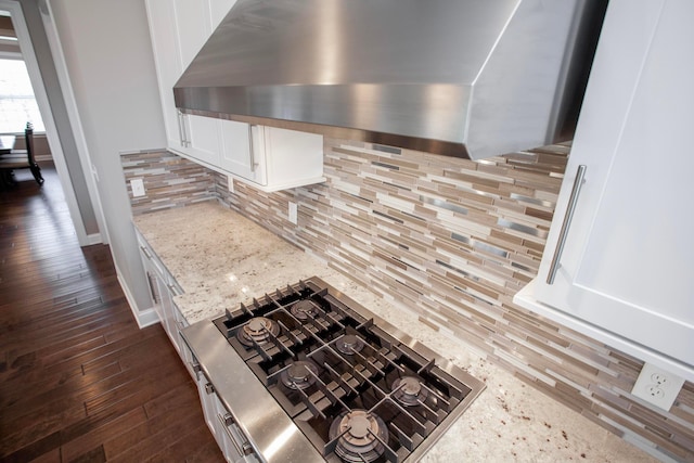 interior details featuring dark wood-type flooring, decorative backsplash, white cabinetry, wall chimney range hood, and cooktop