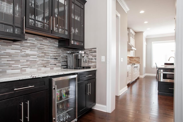 bar with ventilation hood, crown molding, beverage cooler, a dry bar, and stainless steel oven