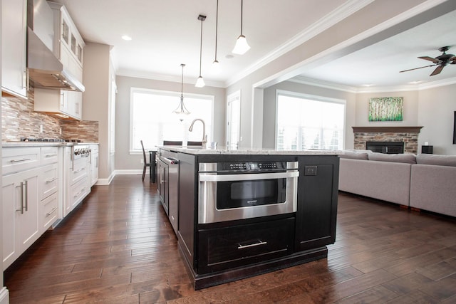 kitchen with dark wood-style floors, a wealth of natural light, wall chimney range hood, and stainless steel oven