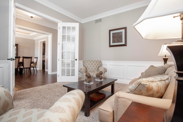 living room with visible vents, a wainscoted wall, carpet floors, ornamental molding, and a decorative wall