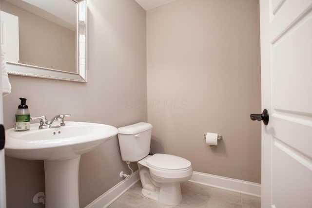 half bath featuring tile patterned flooring, toilet, baseboards, and a sink