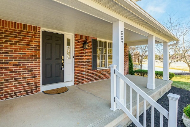 view of exterior entry with brick siding and covered porch