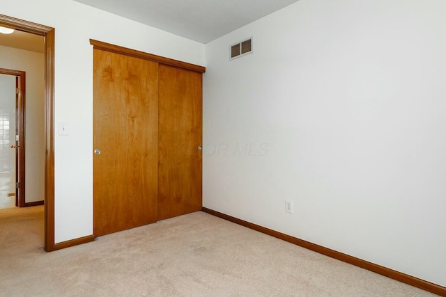 unfurnished bedroom featuring visible vents, baseboards, light colored carpet, and a closet