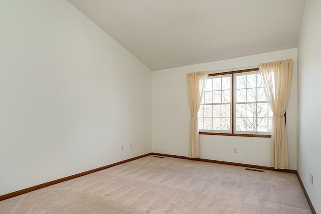 unfurnished room with vaulted ceiling, light colored carpet, visible vents, and baseboards