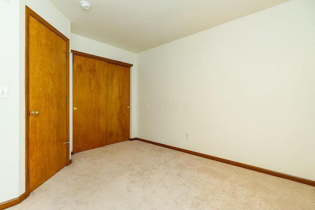 unfurnished bedroom featuring light carpet, baseboards, and a closet