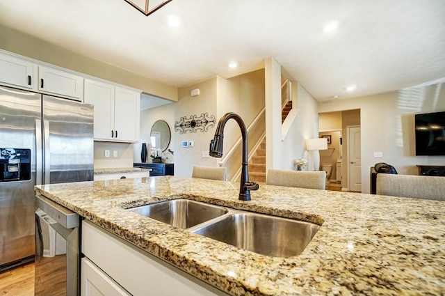 kitchen featuring light stone counters, light wood-style flooring, a sink, white cabinets, and appliances with stainless steel finishes