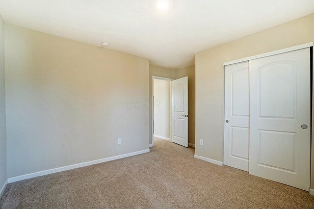 unfurnished bedroom featuring light colored carpet, baseboards, and a closet