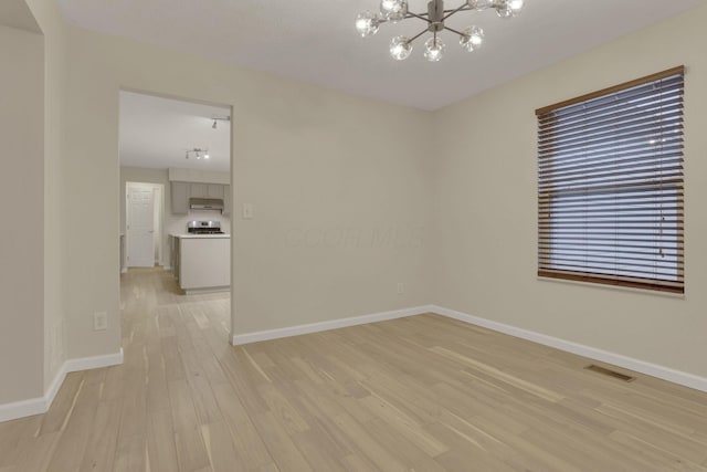 spare room featuring light wood finished floors, visible vents, baseboards, and an inviting chandelier