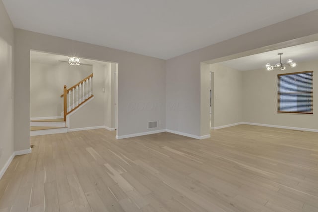 unfurnished room featuring visible vents, a notable chandelier, stairway, and light wood finished floors