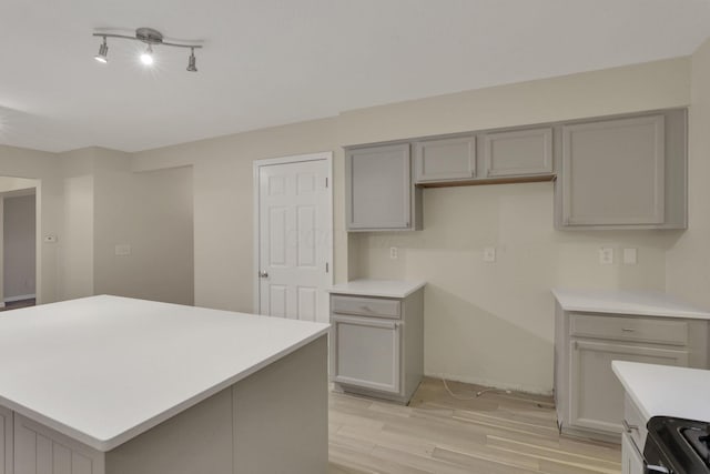 kitchen with a center island, light countertops, light wood-type flooring, gray cabinets, and black range