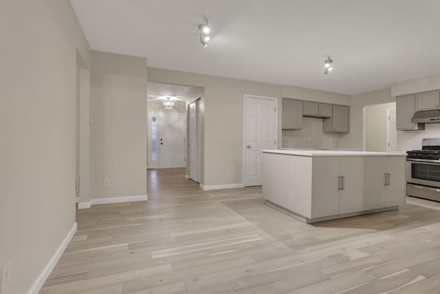 kitchen featuring under cabinet range hood, gas range, gray cabinetry, and light wood-style flooring