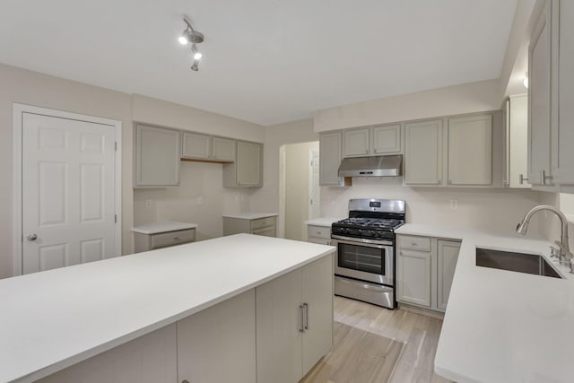 kitchen featuring gray cabinetry, light wood-style flooring, under cabinet range hood, a sink, and gas stove