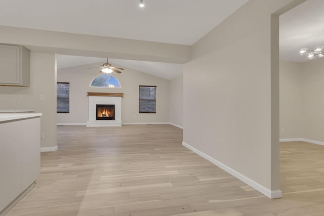 unfurnished living room featuring baseboards, a lit fireplace, vaulted ceiling, light wood-style floors, and a ceiling fan