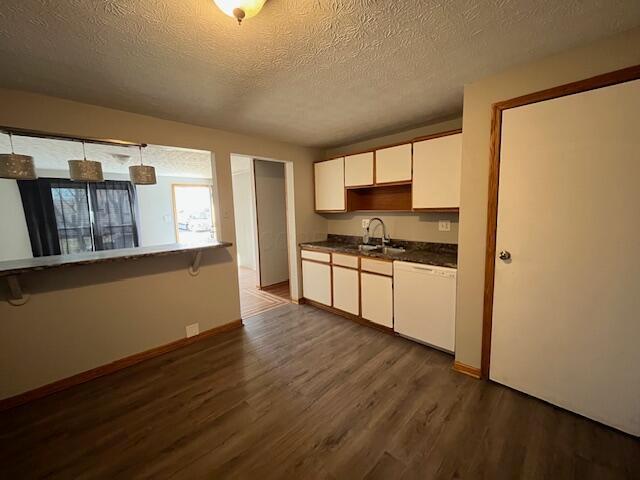 kitchen with dark countertops, dishwasher, dark wood-style floors, white cabinetry, and a sink