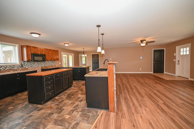 1025 Edison Ave, Marion, OH 43302 - kitchen with black microwave, an island with sink, backsplash, dark cabinets, and butcher block counters