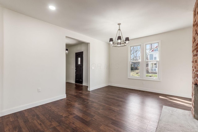 spare room with recessed lighting, baseboards, dark wood-type flooring, and an inviting chandelier