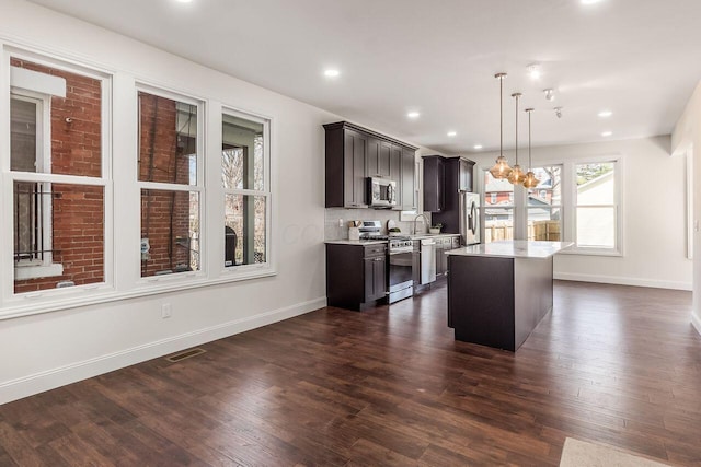 kitchen featuring visible vents, a kitchen island, dark wood-style floors, stainless steel appliances, and light countertops