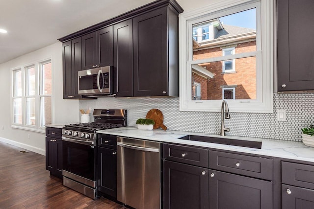 kitchen with backsplash, dark wood-type flooring, light stone countertops, appliances with stainless steel finishes, and a sink