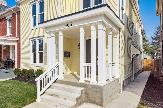 doorway to property with covered porch and fence