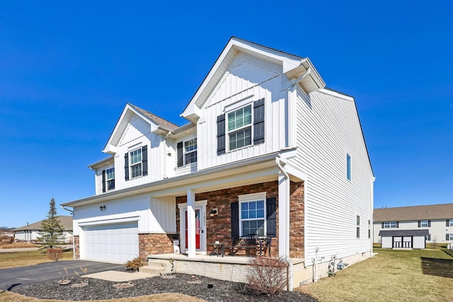 modern inspired farmhouse with a porch, a garage, stone siding, aphalt driveway, and board and batten siding