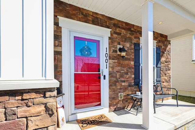 view of exterior entry with brick siding, stone siding, and a porch