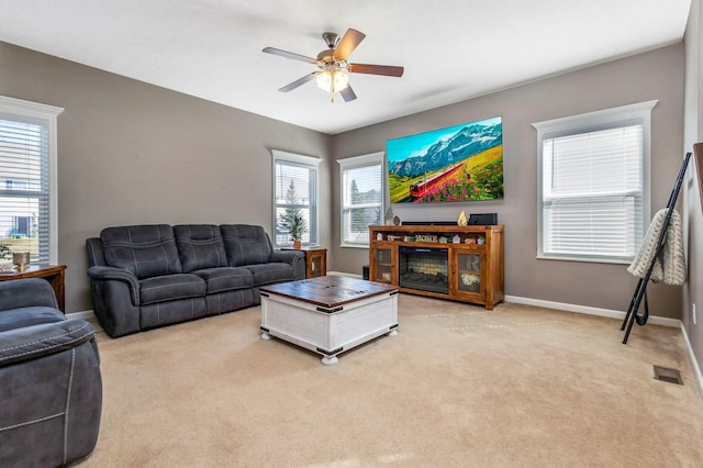 living area with visible vents, light colored carpet, a ceiling fan, and baseboards