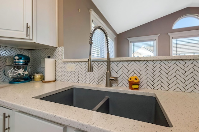 details featuring decorative backsplash, white cabinets, light stone countertops, and a sink