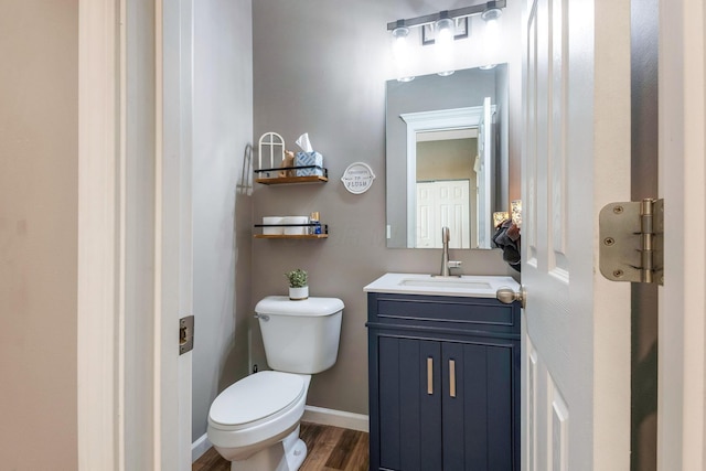 half bath featuring toilet, vanity, baseboards, and wood finished floors