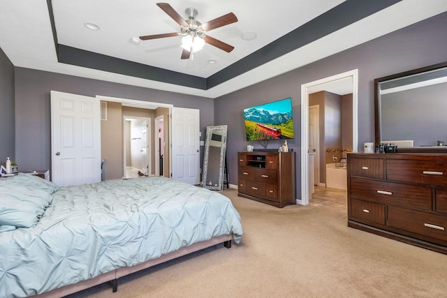 bedroom featuring connected bathroom, light carpet, a raised ceiling, and ceiling fan