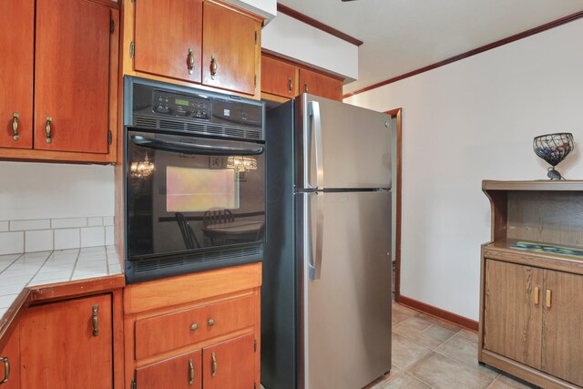 2639 Halleck Dr, Columbus, OH 43209 - kitchen with freestanding refrigerator, black oven, tile counters, brown cabinetry, and ornamental molding
