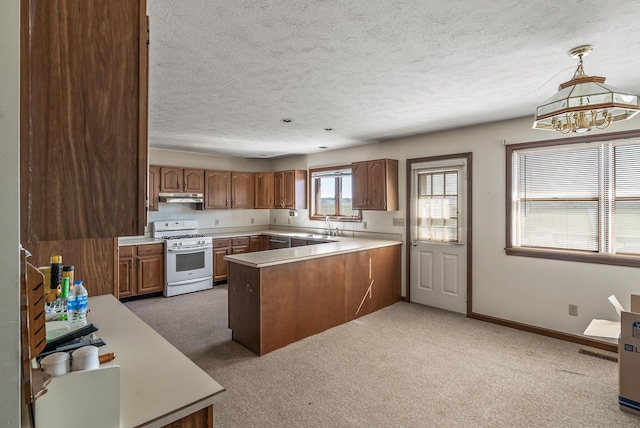 kitchen featuring white range with gas cooktop, brown cabinets, under cabinet range hood, a peninsula, and light countertops