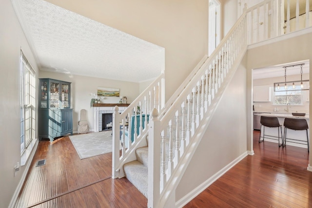 stairway featuring visible vents, baseboards, hardwood / wood-style flooring, a textured ceiling, and a brick fireplace