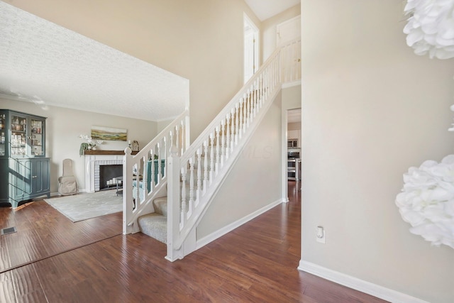 stairway featuring a brick fireplace, baseboards, hardwood / wood-style floors, a towering ceiling, and a textured ceiling