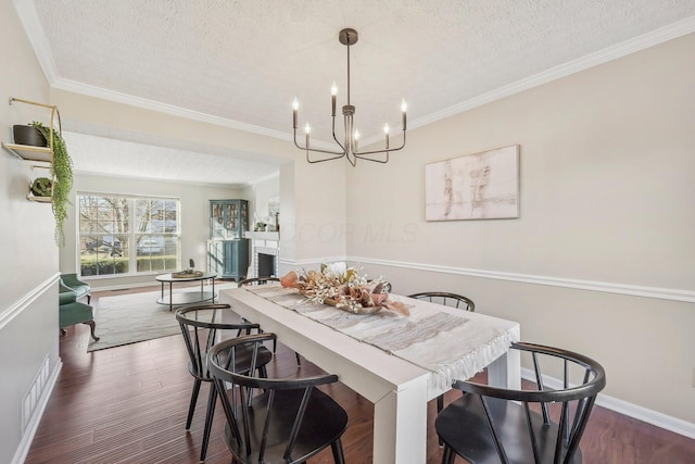 dining space featuring dark wood-type flooring, ornamental molding, a notable chandelier, and a textured ceiling